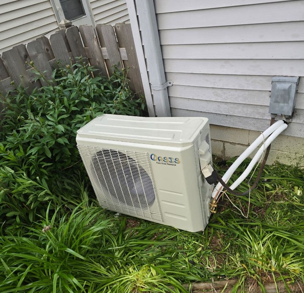 Air conditioning unit installed outside a home, surrounded by green plants and grass.