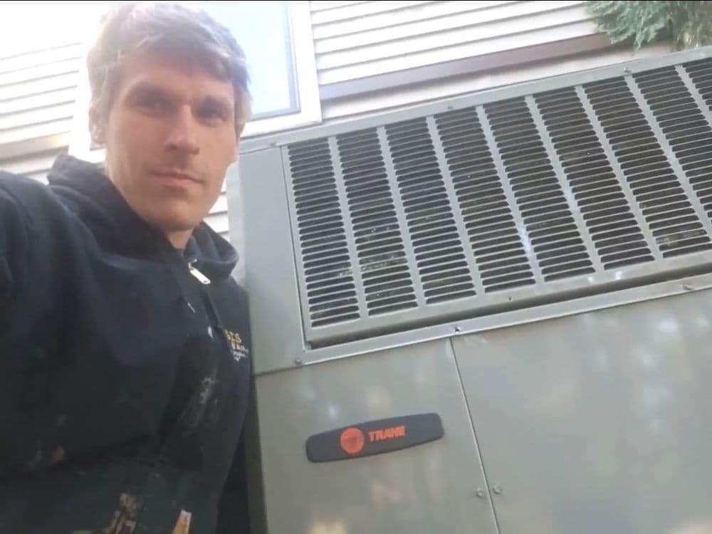 Technician standing next to a Trane HVAC unit during maintenance or installation.