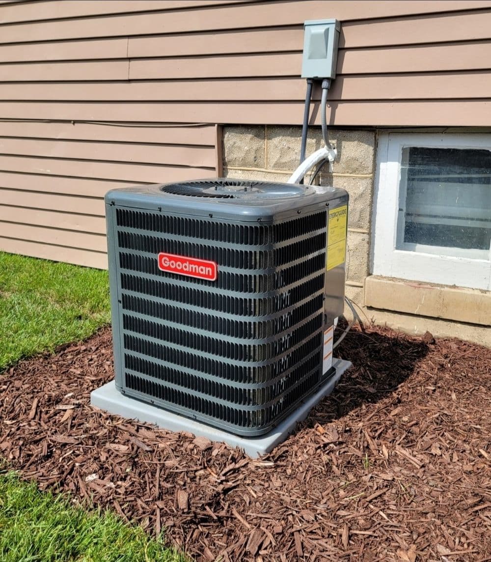 Goodman air conditioning unit installed beside a house on mulch landscaping.